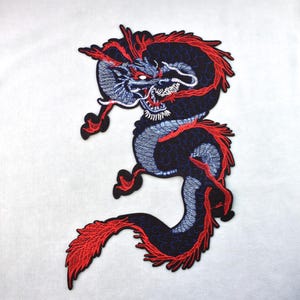 Pode incluir: Patch bordado com um desenho de dragão. O dragão é predominantemente azul marinho com detalhes em vermelho e azul claro. O corpo do dragão é curvo, sobre um fundo branco.