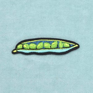 Peut inclure: Un écusson brodé représentant une gousse de petits pois avec une bordure noire. La gousse est ouverte, révélant sept petits pois vert vif à l'intérieur. L'intérieur est bleu foncé, tandis que l'extérieur est bleu clair avec des reflets jaunes.