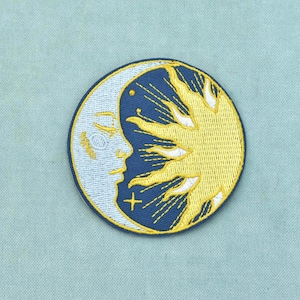 Könnte beinhalten: Ein kreisförmiger bestickter Aufnäher mit einem hellblauen Halbmond mit menschlichem Gesichtsprofil auf der linken Seite, kontrastiert durch einen dunkelblauen Hintergrund mit einem leuchtend gelben Sonnendesign auf der rechten Seite.
