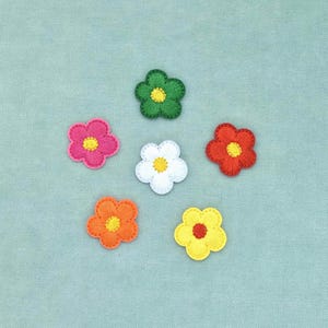 Op de afbeelding: Een verzameling van zes kleine, vijfbladige bloemapplicaties gerangschikt in een cirkelvormig patroon. De applicaties zijn gemaakt van geborduurde stof in verschillende kleuren: groen, roze, wit, rood, oranje en geel, elk met een contrasterende kleur in het midden.