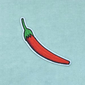 Pode incluir: Um emblema bordado em forma de pimenta com um corpo vermelho brilhante e um caule verde. O emblema apresenta uma borda branca e é projetado com costuras detalhadas para criar uma aparência texturizada da superfície do vegetal.