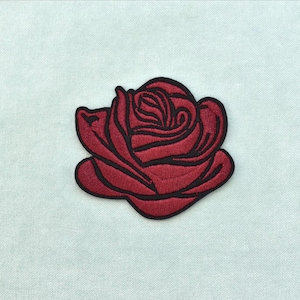Peut inclure: Un écusson de rose rouge avec un contour noir, sur fond bleu clair. Le patch brodé présente un motif de rose détaillé, idéal pour les vêtements ou les accessoires.