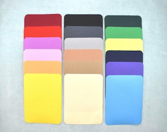 May include: A selection of rectangular colour swatches with rounded corners, presented in three columns. The swatches display a range of hues, including red, orange, yellow, black, grey, beige, green, blue, and purple. The background is a pale, neutral shade.