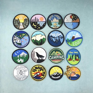 Puede incluir: Una colección de dieciséis parches bordados circulares con temas de naturaleza y aire libre. Los diseños incluyen montañas, bosques, escenas de camping, la silueta de un lobo, una brújula y olas, con textos como Camping y Wanderer.