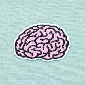 Peut inclure: Un écusson brodé en forme de cerveau humain. Le motif présente du fil rose clair pour le tissu cérébral et du fil noir épais pour les motifs complexes et sinueux des sillons et des circonvolutions, le tout bordé d'un contour blanc net.