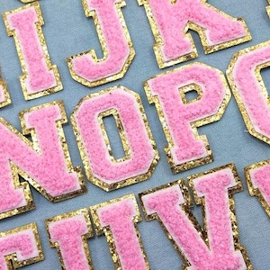 Peut inclure: Écussons de lettres en chenille rose avec des bordures dorées à paillettes. Les lettres sont de style universitaire, parfaites pour personnaliser des vêtements ou des accessoires. L'image montre diverses lettres, dont M, N, O, P, Q, R, T, V et W.