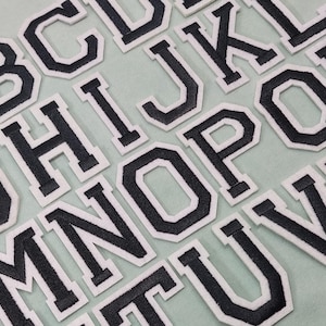 Puede incluir: Letras del alfabeto de fieltro negro con contorno blanco. Las letras están dispuestas en orden alfabético.