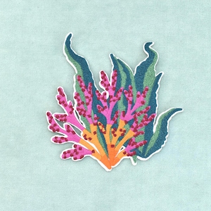Op de afbeelding: Een geborduurde patch met een gestileerd ontwerp van een waterplant. De patch toont donkergroene, golvende, bladachtige bladeren achter felroze, vertakte, koraalachtige structuren die uit een effen oranje basis aan de onderkant komen.