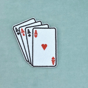 Puede incluir: Un parche bordado que muestra un abanico de cuatro cartas de juego, específicamente los cuatro ases. Cada carta es blanca con un borde negro, mostrando la letra A y el símbolo del palo correspondiente en hilo rojo o negro en la cara.
