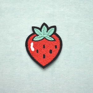 Peut inclure: Écusson brodé en forme de fraise, avec un corps rouge, des graines noires et des feuilles vertes. L'écusson a une bordure noire et un reflet blanc. L'écusson est sur un fond bleu clair.