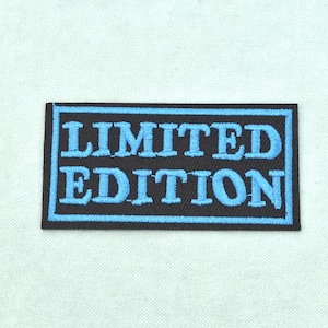 Peut inclure: Un écusson rectangulaire brodé présentant un fond noir avec une bordure bleu clair et le texte LIMITED EDITION cousu en lettres capitales bleu clair. L'écusson possède un bord fini net et un aspect de tissu texturé.