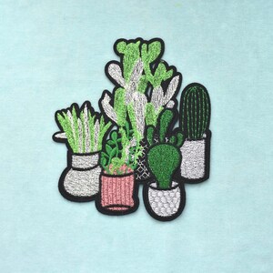 Pode incluir: Patches bordados com vários cactos e suculentas em vasos. Os patches apresentam uma variedade de plantas verdes com detalhes em branco e preto. Os patches são delineados em preto e estão sobre um fundo azul claro.