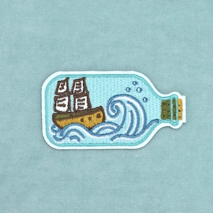 Op de afbeelding: Een geborduurde patch met een bruin schip met witte zeilen in de vorm van een lichtblauwe glazen fles. Het ontwerp bevat gestileerde blauwe oceaangolven en kleine belletjes, allemaal omlijnd met wit garen op een lichtblauwe achtergrond.