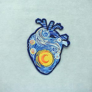 May include: Embroidered patch in the shape of a human heart, featuring a design inspired by Van Gogh's "Starry Night." The patch has a blue outline, with swirling blue and white details, and a yellow and orange crescent moon.