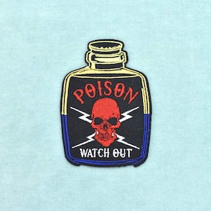 Peut inclure: Un écusson brodé en forme de bouteille avec un fond noir et bleu. Il présente un crâne rouge au centre, deux éclairs blancs, le texte rouge POISON au-dessus du crâne et le texte blanc WATCH OUT en dessous du crâne.