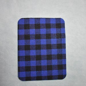 Puede incluir: Un posavasos de tela a cuadros azules y negros. El posavasos es rectangular y tiene una superficie suave y texturizada.