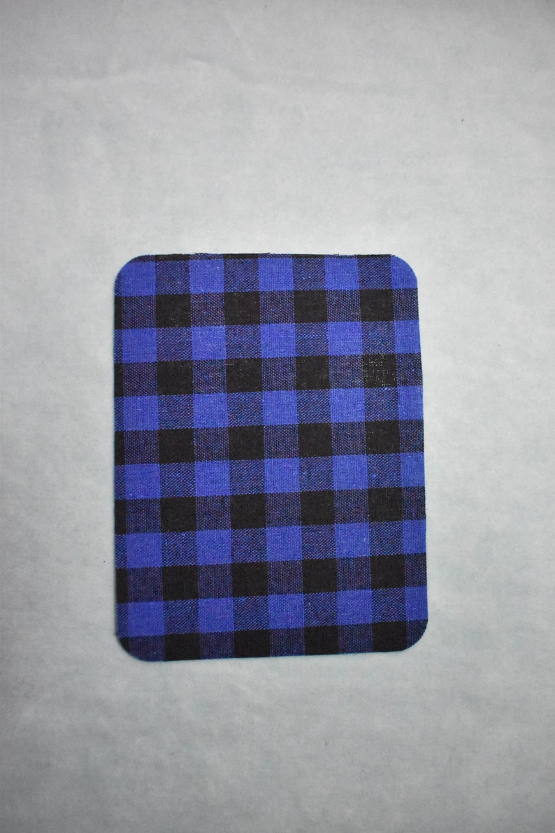Puede incluir: Un posavasos de tela a cuadros azules y negros. El posavasos es rectangular y tiene una superficie suave y texturizada.