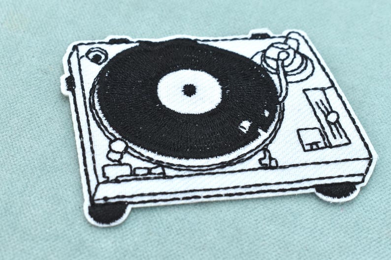 May include: A rectangular embroidered patch featuring a black and white line art design of a turntable. The patch displays a central black vinyl record on a white base with detailed outlines of the tonearm, platter, and control knobs.