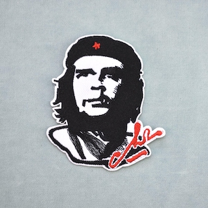 Könnte beinhalten: Gestickter Aufnäher mit einem schwarz-weißen Porträt von Che Guevara, der eine Baskenmütze mit einem roten Stern trägt. Der Aufnäher enthält eine rote Unterschrift. Der Aufnäher befindet sich auf einem hellgrauen Hintergrund.