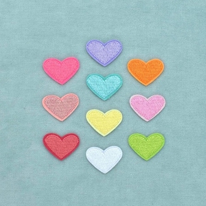 Op de afbeelding: Een verzameling van tien geborduurde hartvormige patches gerangschikt in een rasterpatroon. De harten hebben verschillende effen kleuren, waaronder lavendel, oranje, roze, taling, geel, rood, limoengroen en wit, elk met een gestikte rand.