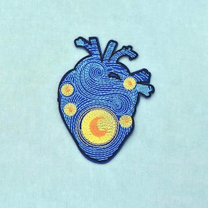 Puede incluir: Un parche bordado con forma de corazón anatómico, que presenta un fondo azul oscuro con patrones de hilo azul claro en espiral, acentuado por varias estrellas circulares amarillas y una luna amarilla central con una media luna naranja.