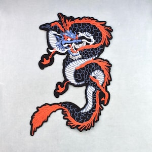 Könnte beinhalten: Ein gestickter Aufnäher mit einem stilisierten Drachen in eingerollter Position. Der Drache hat einen dunkelblauen Körper mit schwarzen Schuppen, leuchtend orangefarbene Mähnen- und Schwanzakzente sowie einen weißen Bauch. Das Motiv hat einen dicken schwarzen Rand.