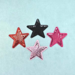 Può includere: Quattro toppe a forma di stella ricoperte di paillettes. Una toppa è nera, una è rosso brillante, una è rosa acceso e una è di una tonalità di rosa più chiara. Ogni stella ha un bordo in tessuto abbinato che crea un contorno distinto.
