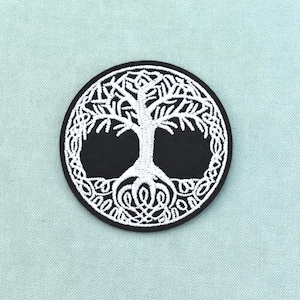 Puede incluir: Un parche bordado circular que presenta un diseño de árbol de la vida en blanco con intrincadas raíces y ramas entrelazadas sobre un fondo negro sólido. El bordado es denso y texturizado, creando un contraste claro entre el hilo blanco y la base de tela negra del parche.
