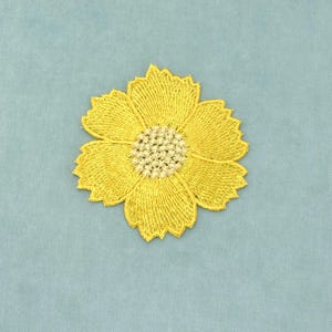 Peut inclure: Un écusson brodé en forme de fleur jaune avec six pétales aux bords dentelés et un centre circulaire texturé de couleur claire. La broderie se compose de fils denses et rayonnants qui forment une silhouette florale bien définie.
