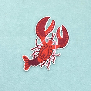 Peut inclure: Un écusson brodé thermocollant représentant un homard rouge vif avec des nuances rouge foncé sur la queue et les pinces. Le homard est illustré avec deux grandes pinces, plusieurs pattes et de longues antennes fines rose clair, le tout bordé de blanc.
