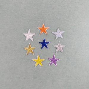 Könnte beinhalten: Eine Sammlung von acht gestickten Sternaufnähern in verschiedenen Farben, darunter Weiß, Orange, Blau, Gold, Gelb und Lila. Jeder Stern hat einen weißen Rand und ist auf einem hellgrünen Hintergrund kreisförmig angeordnet. Diese Aufnäher eignen sich zur Stoffdekoration.