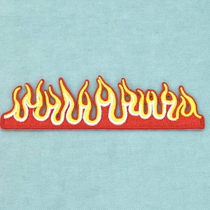 Peut inclure: Un écusson brodé représentant une rangée horizontale de flammes stylisées. Le motif se compose d'une base rouge unie avec des contours en forme de flammes jaunes et blanches superposés, créant un élément graphique coloré pour tissu.