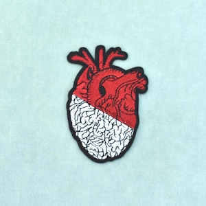 May include: An embroidered patch featuring an anatomical heart design. The upper portion is rendered in red thread with detailed vascular structures, while the lower portion is white with a textured pattern resembling brain matter, all outlined in black.