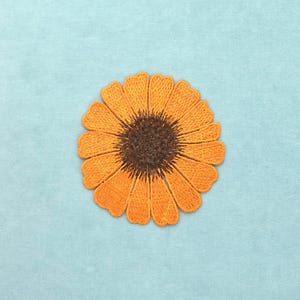 Peut inclure: Un écusson brodé circulaire représentant une fleur stylisée avec des pétales orange vifs rayonnant depuis un centre texturé brun foncé. La broderie est dense et uniforme, créant une forme florale nette aux bords bien définis.