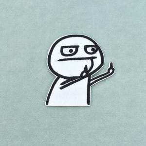 Pode incluir: Um emblema bordado branco com uma ilustração de linhas pretas de uma personagem de desenho animado com uma expressão cética, uma mão levada ao queixo e a outra mão fazendo um gesto de dedo médio sobre um fundo branco sólido.