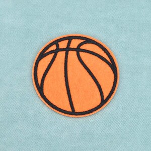 Op de afbeelding: Een ronde geborduurde patch met een basketbalontwerp. De patch is feloranje met dikke, donkerzwarte gestikte lijnen die het klassieke patroon van een basketbal vormen, wat zorgt voor een getextureerd en duidelijk gedefinieerd uiterlijk.