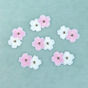 Peut inclure: Six écussons brodés en forme de fleurs, chacun composé de deux fleurs en fil rose pâle et blanc. Chaque fleur possède cinq pétales avec un détail central marron foncé. Ces petites applications décoratives en tissu sont disposées en éparpillement.