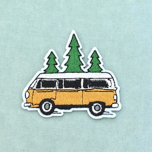 Op de afbeelding: Een geborduurde patch met een gele camper met een wit dak. Bovenop de camper staan drie groene dennenbomen. Het ontwerp is omlijnd met wit garen, wat een duidelijke vorm creëert tegen de lichtblauwe stoffen achtergrond van de afbeelding.
