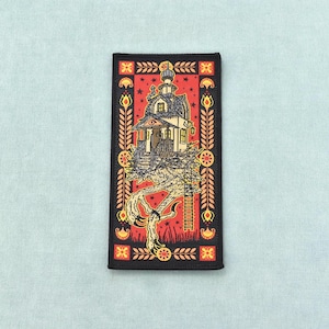 Peut inclure: Un écusson rectangulaire brodé représentant une maison perchée sur une griffe d'oiseau géante sur fond rouge. Le motif inclut une échelle, des étoiles et une bordure décorative avec des motifs floraux jaunes, le tout dans un cadre noir.