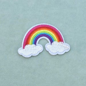 Peut inclure: Un écusson brodé thermocollant représentant un arc-en-ciel vibrant au-dessus de deux nuages blancs. L'arc-en-ciel est composé de bandes horizontales de fils rouge, orange, jaune, vert, bleu et violet, avec des nuages blancs aux extrémités.