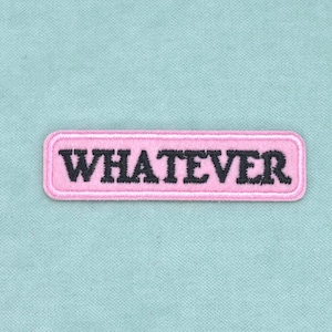 Peut inclure: Un écusson rectangulaire brodé présentant un fond rose clair avec une bordure cousue et le mot WHATEVER écrit en lettres capitales noires et grasses. L'écusson est centré sur une surface en tissu bleu clair avec un tissage texturé.