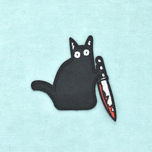 Peut inclure: Un écusson brodé représentant un chat noir stylisé aux grands yeux blancs. Le chat est représenté en position assise, tenant un couteau de couleur argentée avec une lame à pointe rouge dans l'une de ses pattes avant sur un tissu bleu clair.
