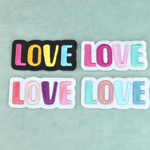 Puede incluir: Cuatro parches rectangulares bordados con la palabra LOVE en letras negritas, redondeadas y sin remates. Cada parche muestra una combinación de colores única de rosa, amarillo, azul, morado y melocotón, con bordes de tela negros o blancos.