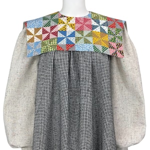May include: A long-sleeved dress with a black and white checkered pattern. The dress has a large, colorful patchwork collar with a geometric design.