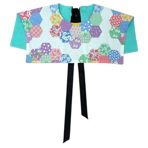 May include: A white crop top with a patchwork design of colourful hexagons. The top has short sleeves and a black ribbon tie at the back.