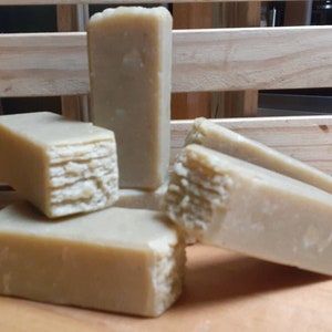 May include: Five bars of handmade soap, each with a light brown color and a textured surface. The bars are stacked on top of each other, with one bar partially visible in the background.