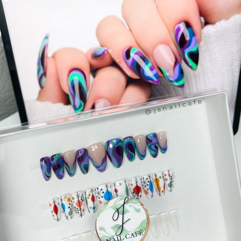 Puede incluir: Conjunto de u&ntilde;as postizas con dos dise&ntilde;os diferentes. Un conjunto presenta un patr&oacute;n de espiral en tonos de morado, verde y negro. El otro conjunto presenta una base blanca con formas geom&eacute;tricas coloridas. Las u&ntilde;as se muestran en una caja de pl&aacute;stico transparente con el texto "@jsnailcafe" y "Nail Cafe" impreso en ella.