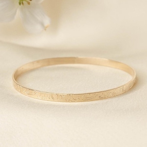 May include: A gold bangle bracelet with a delicate floral design engraved around the band.