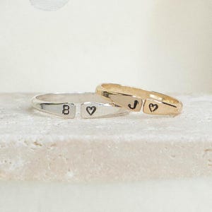 May include: Two silver rings with a heart and letter 'B' on one ring and a heart and letter 'J' on the other ring.