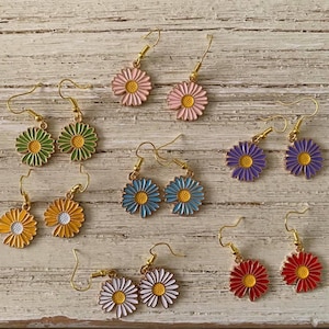 May include: Assortment of colorful daisy flower earrings with gold hooks. The earrings are in various colors including pink, green, blue, purple, white, and red.